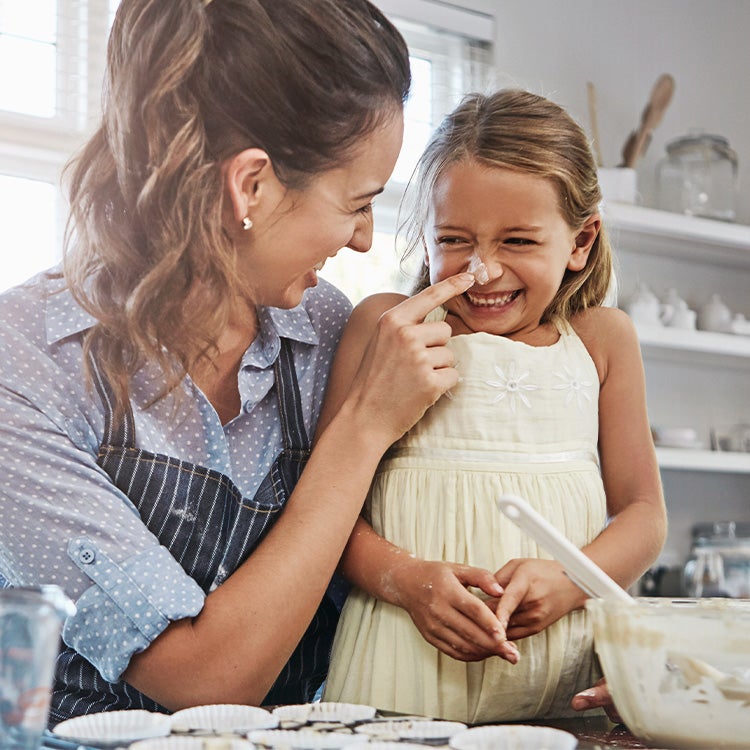 A parent and child enjoying family baking time together as guardian dots child’s nose with flour