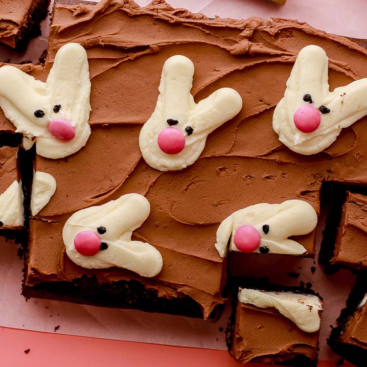 Rectangular chocolate buttercream topped cake with buttercream bunnies, with pink candy noses and small black eyes.