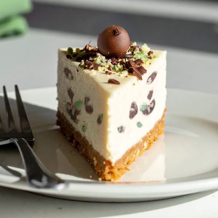 Slice of mint Aero cheesecake with chocolate shavings and biscuit base on a white plate in natural light