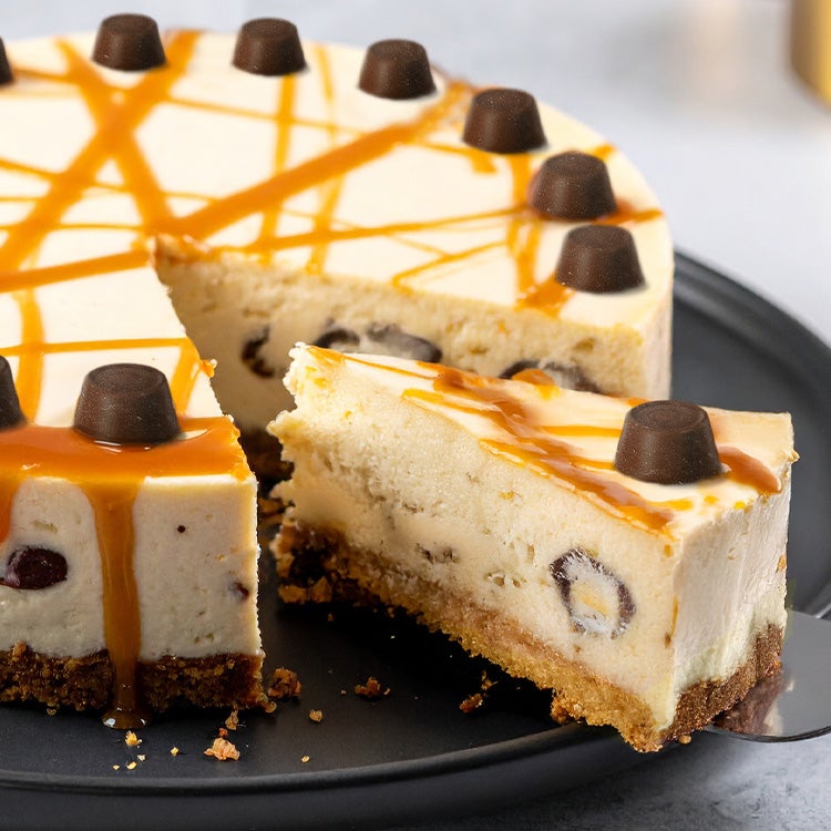 Whole Rolo caramel cheesecake with a slice being served, topped with Rolo chocolates and caramel drizzle on a black plate