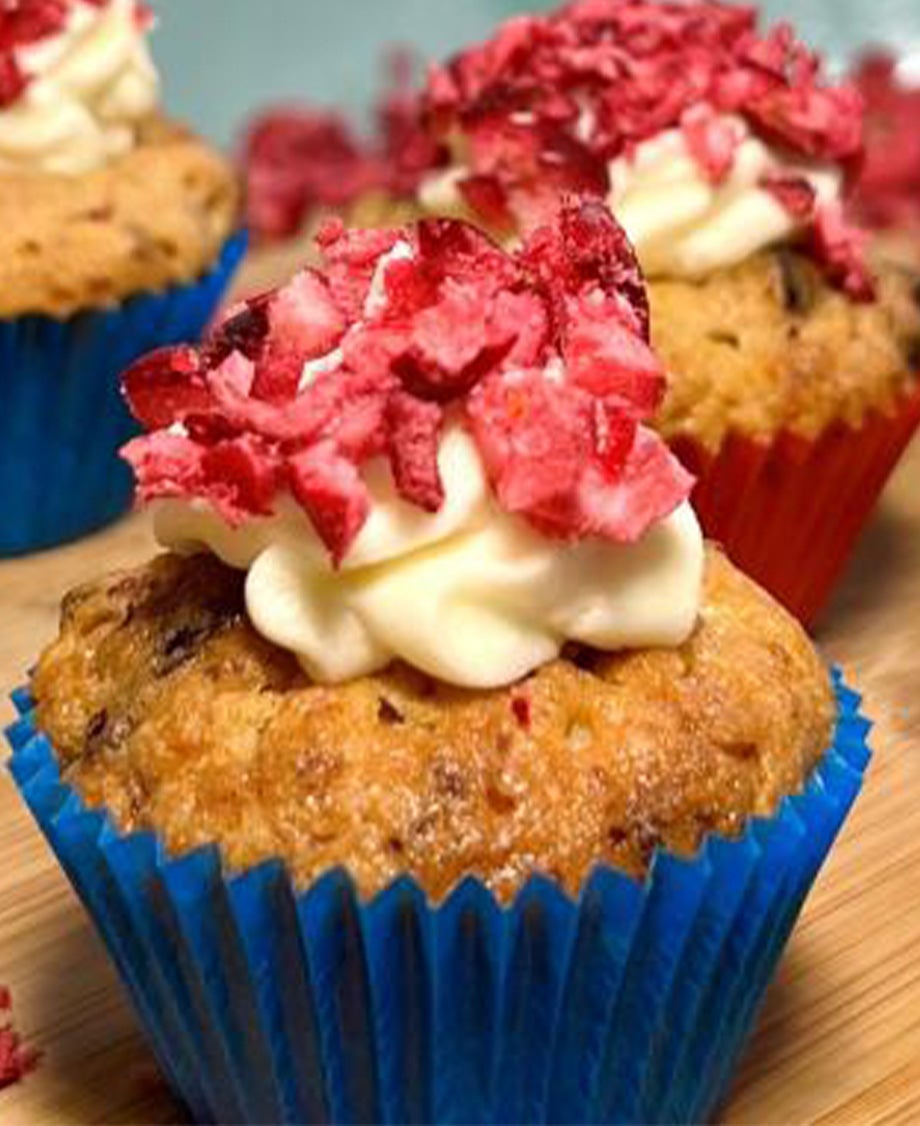 Light-coloured white chocolate & cranberry muffin topped with a swirl of icing & a pinch of dried cranberries in a blue case.