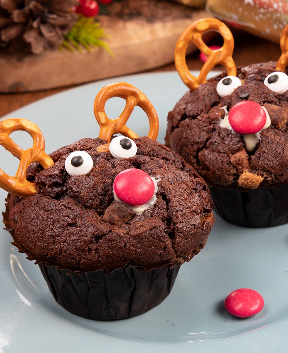 Chocolate muffins decorated like reindeers with pretzels for ears, a red Smartie for a nose and googly eyes.