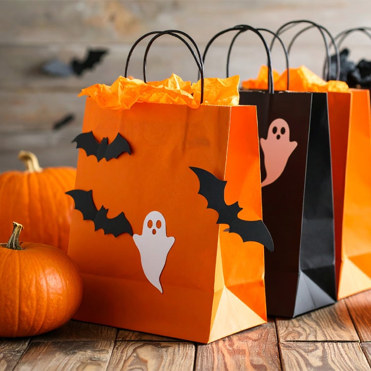 Selection of Halloween themed paper party bags on a wooden table surrounded by pumpkins