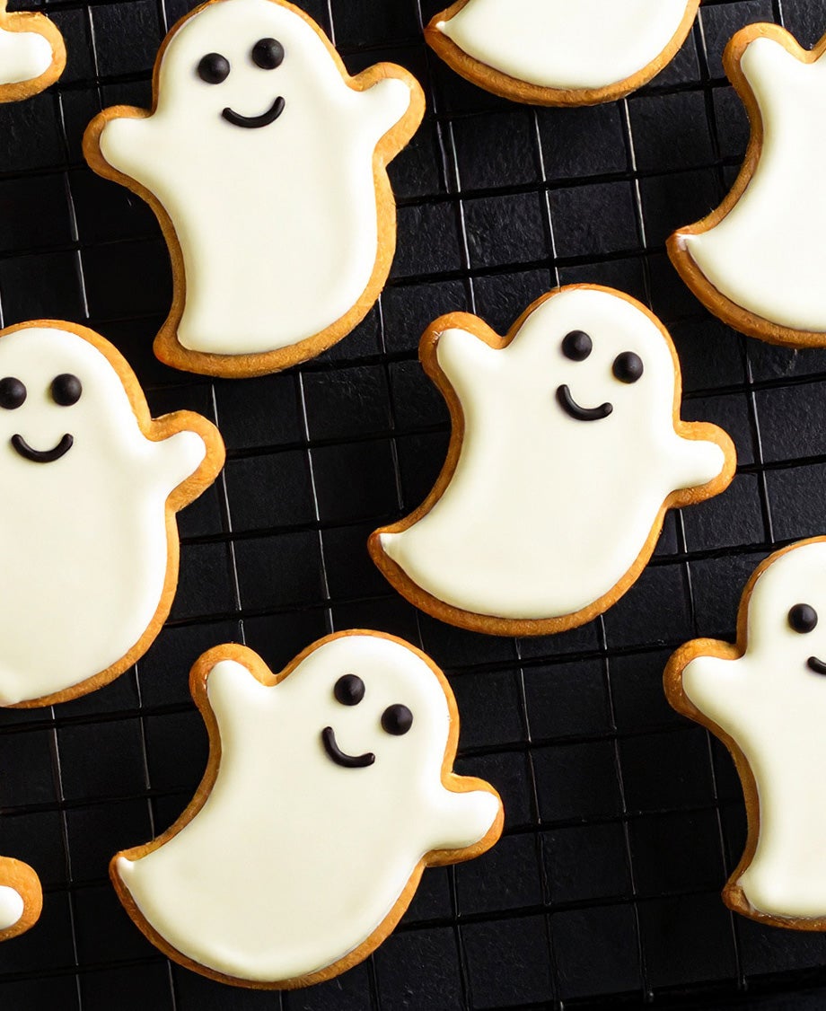 Friendly looking ghost-shaped cookies on a black wire rack