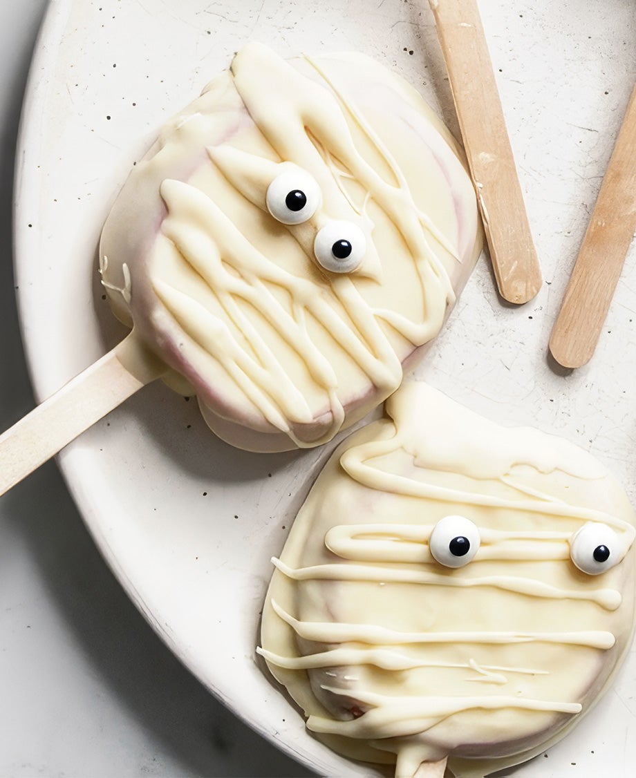 Milkybar-dipped mummy apple slice pops with googly eyes and white chocolate drizzle on sticks