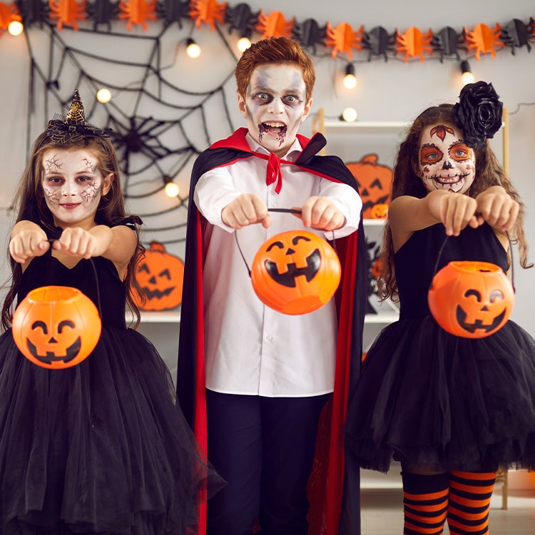 Group of children dressed in Halloween fancy dress holding plastic pumpkin-face sweets buckets ready to fill on trick or trea