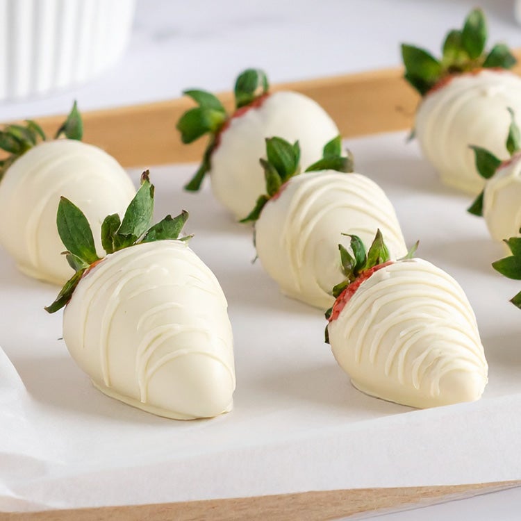 Fresh strawberries dipped in white chocolate on a wooden tray with more fresh strawberries scattered around
