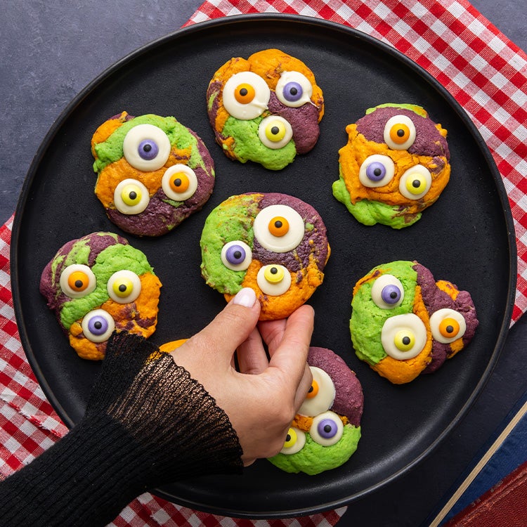 Orange, green and purple monster cookies with three Milkybar white chocolate googly eyes with purple, yellow and orange Smart