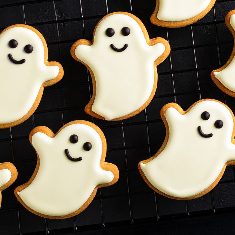 Homemade Halloween Ghost Cookies with Milkybar white chocolate icing and smiling faces, cooling on a black wire rack
