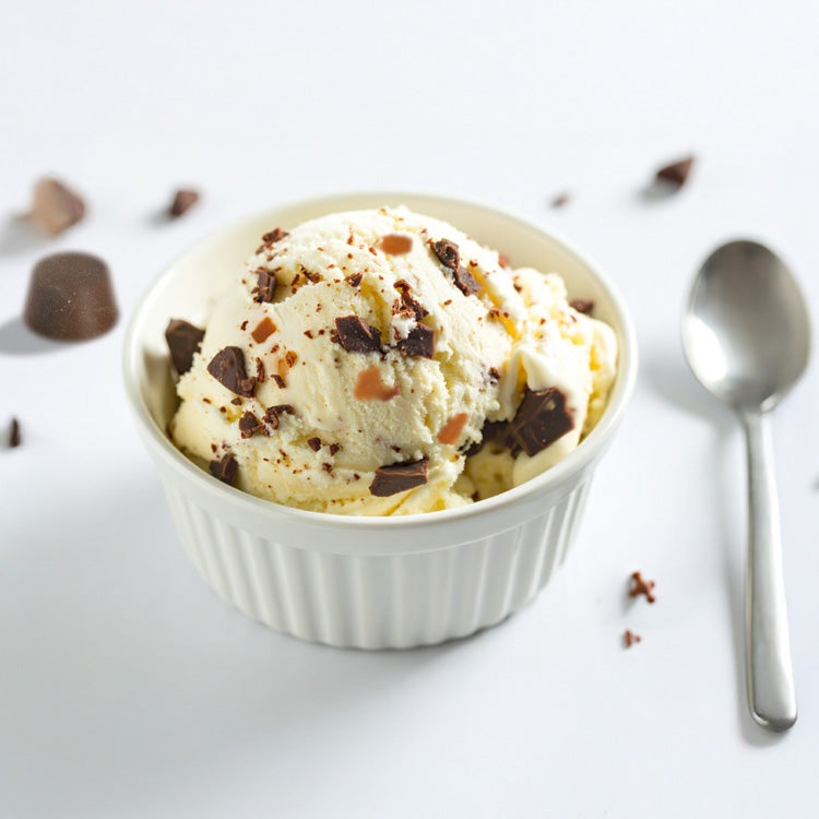 One scoop of cream-coloured ice cream in a bowl, studded with chocolate and caramel with a spoon next to it and a rolo in the