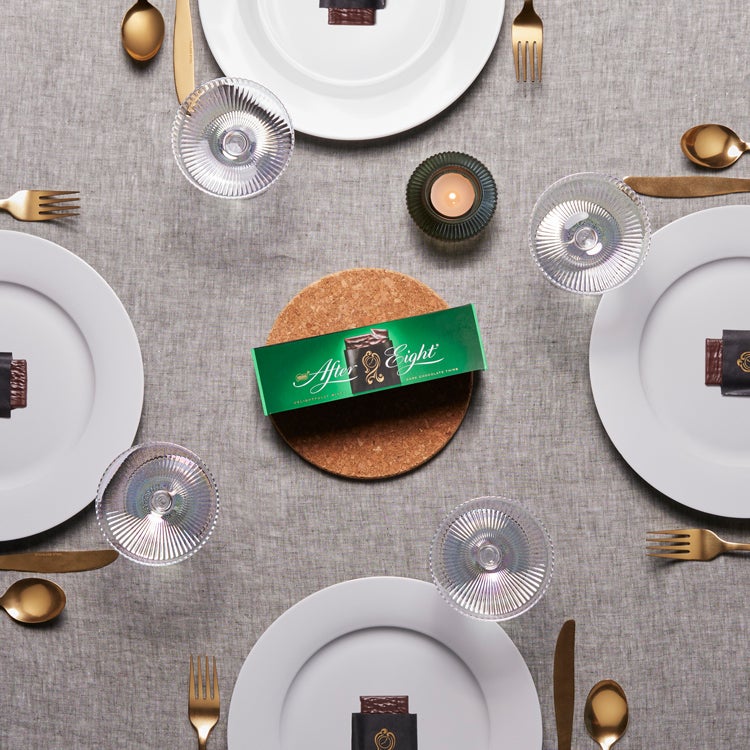 Overhead shot of a round dinner table with linen tablecloth set for four, with an After Eight mint chocolate on each plate an