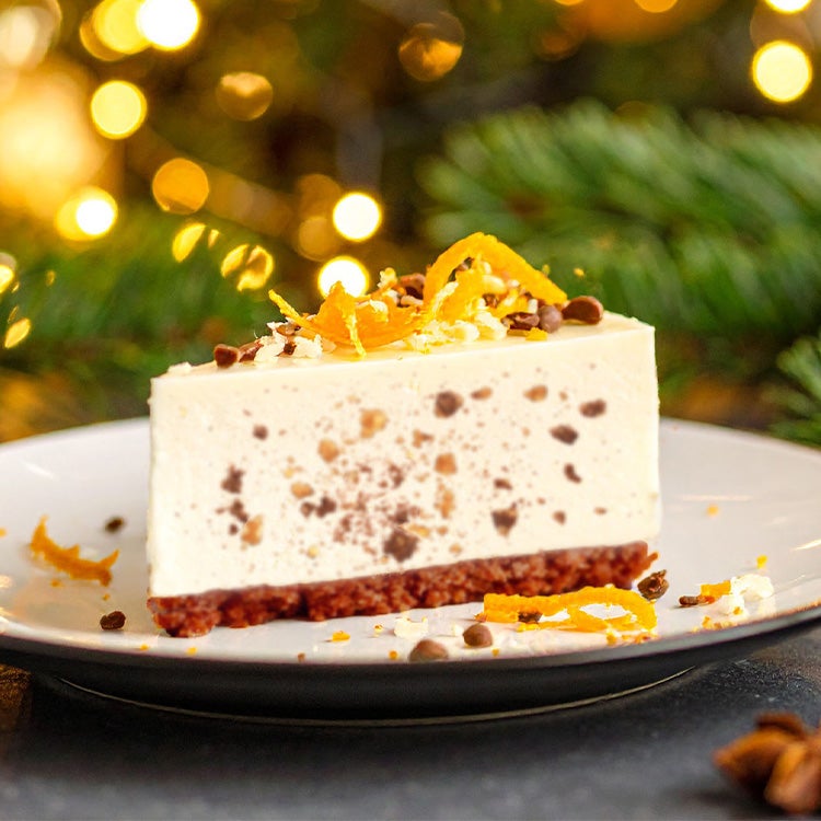 Slice of orange and mincemeat cheesecake on a plate with pine cones, dried orange slices, fir sprigs and Christmas lights in 