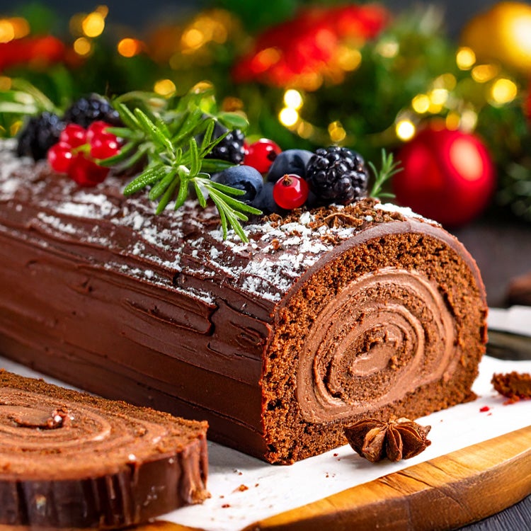 Chocolate yule log made with Aero on a wooden board decorated with rosemary sprigs, forest berries and a dusting of icing sug