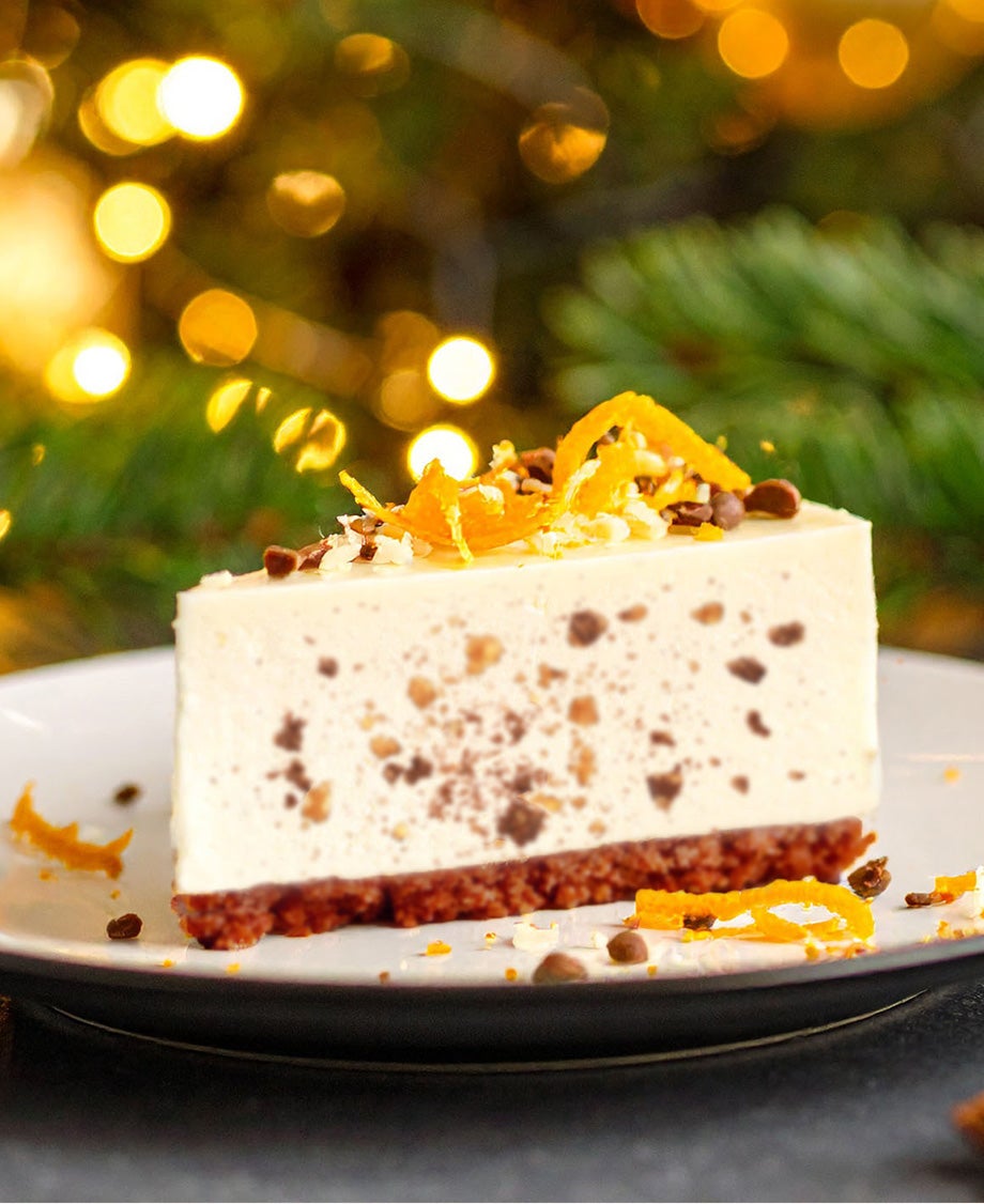 Slice of orange and fruit mincemeat cheesecake on plate with pine cones, dried orange slices, fir sprigs and Christmas lights