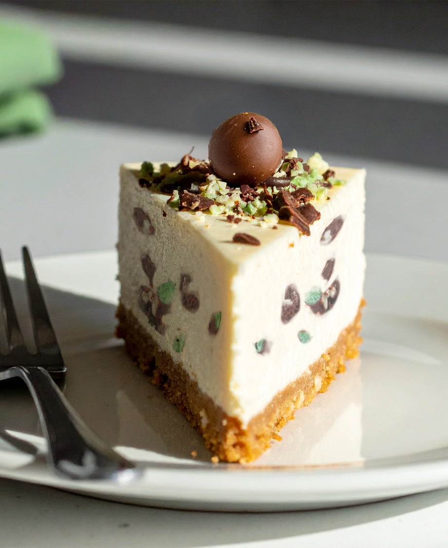 Slice of mint Aero cheesecake with chocolate shavings and biscuit base on a white plate in natural light