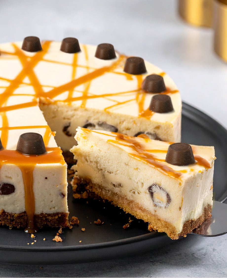 Whole Rolo caramel cheesecake with a slice being served, topped with Rolo chocolates and caramel drizzle on a black plate
