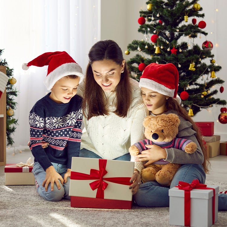 A mother and her two children in a white minimalist living room opening a Christmas Ever Box and looking inside with Christma
