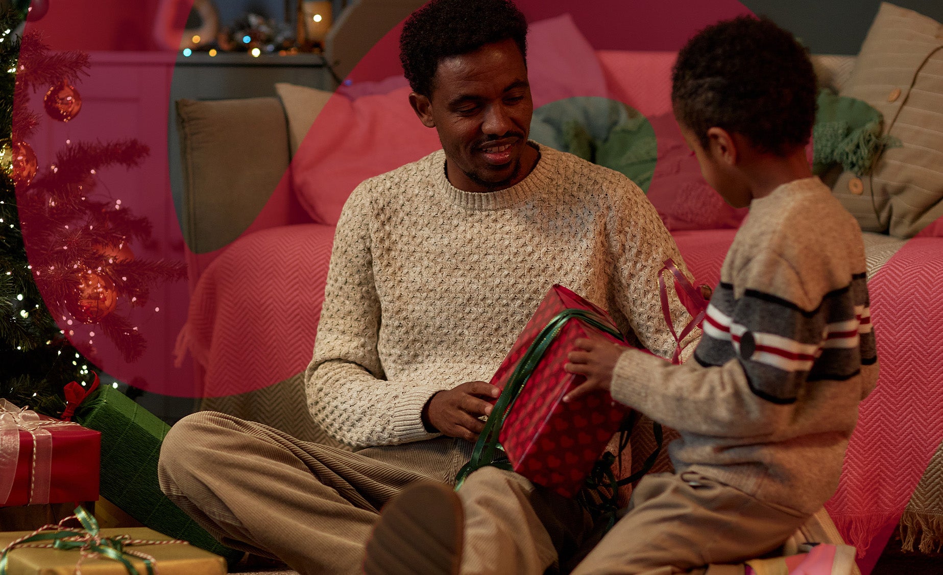A father and son in a cosy living room with Christmas decorations, opening a festive wrapped box