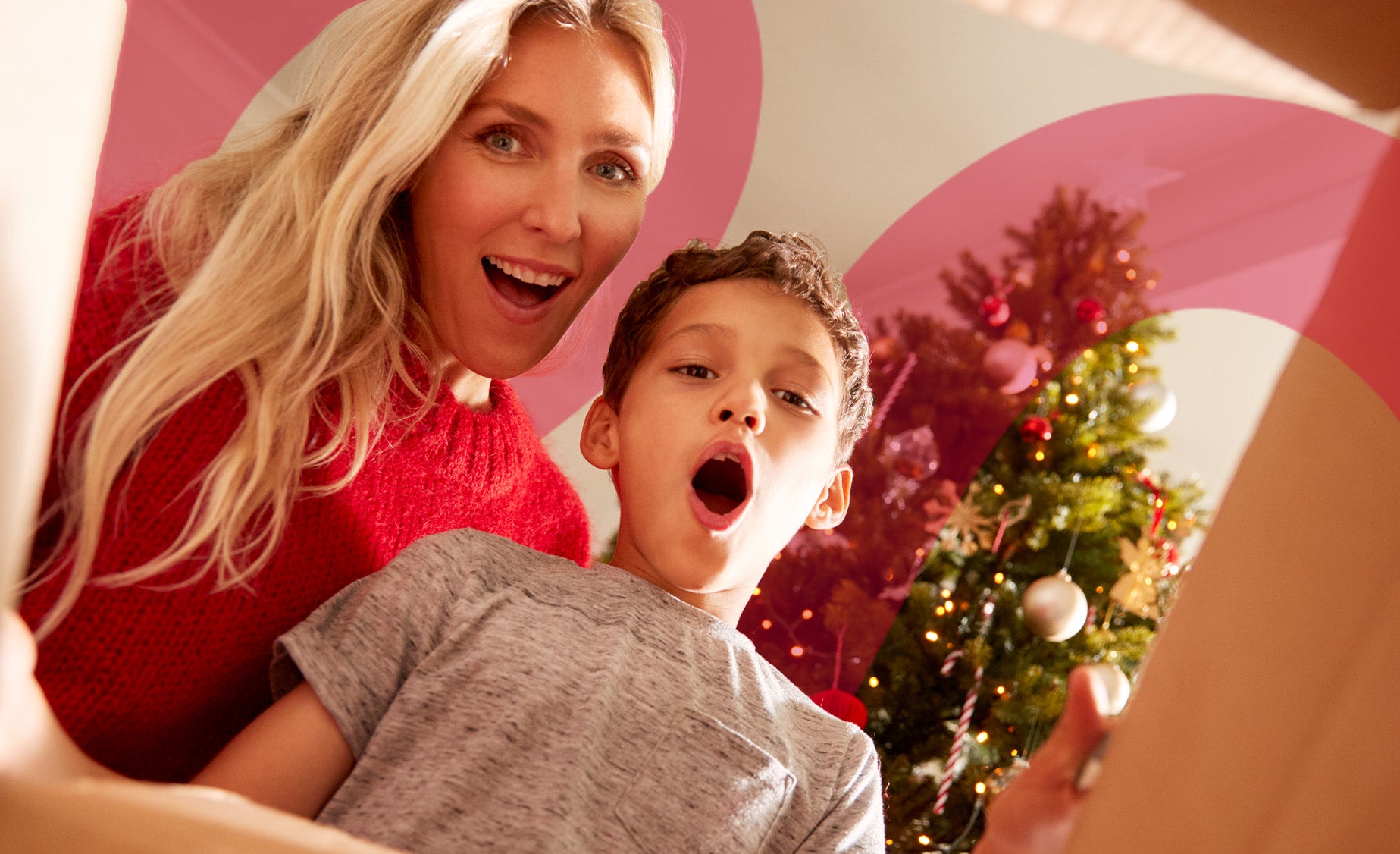  A mother and son in a Christmassy living room look at the camera in open-mouthed delight and surprise