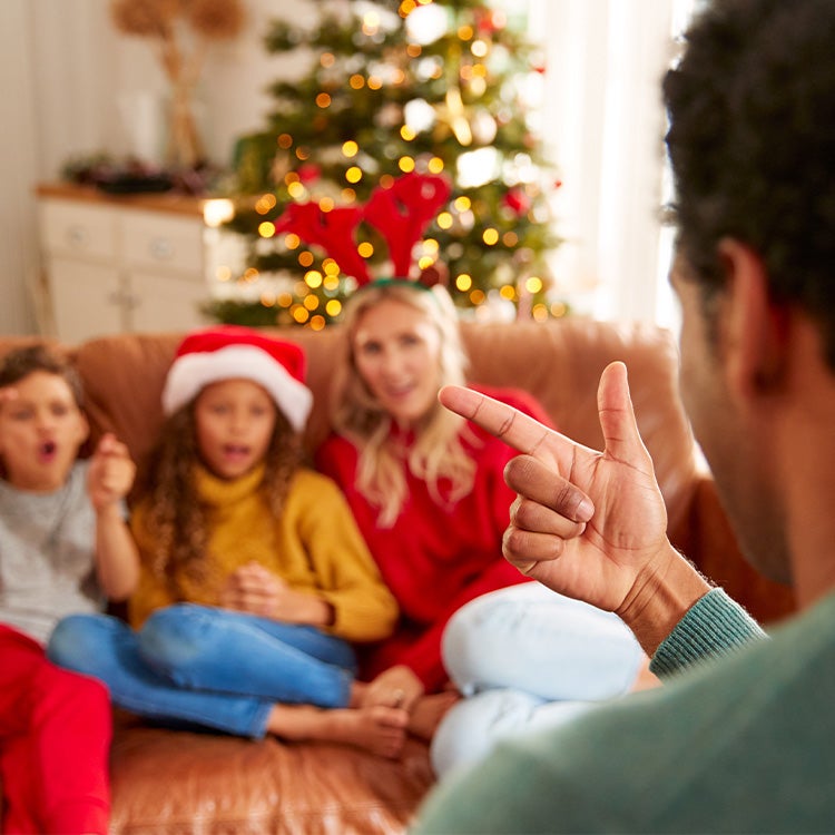 A family sat on a comfy leather sofa with Christmas tree in the background, taking part in a Christmas quiz