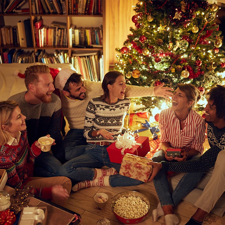 Group of friends in a cosy living room at Christmas, opening presents together while laughing