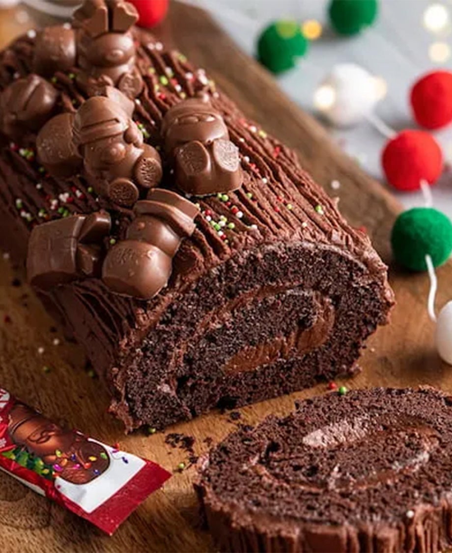 A rich yule log decorated with KitKat Festive Friends on a wooden chopping board.