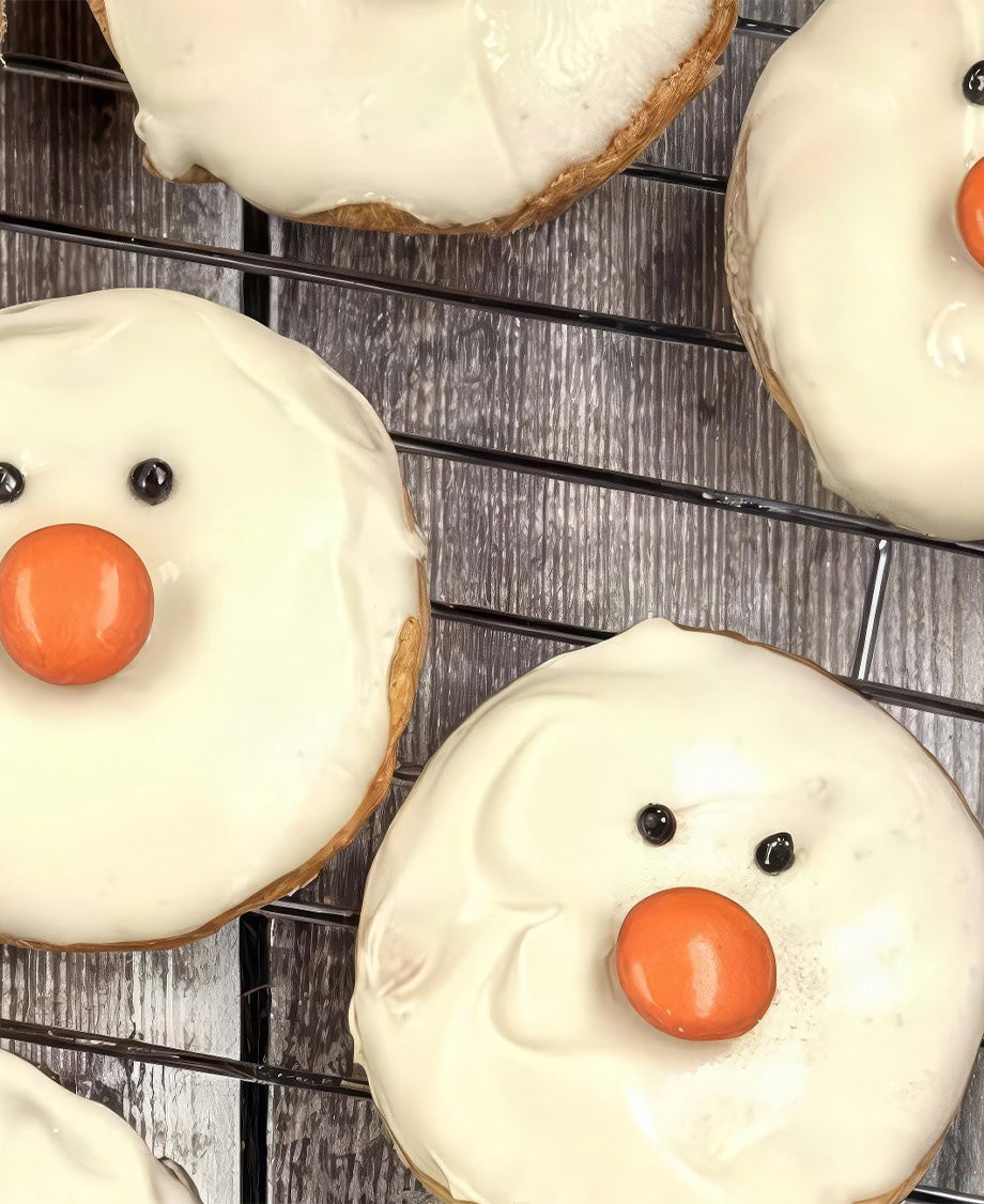 Round shortbread biscuits decorated with Milkybar white chocolate faces and orange Smarties noses on a wire rack