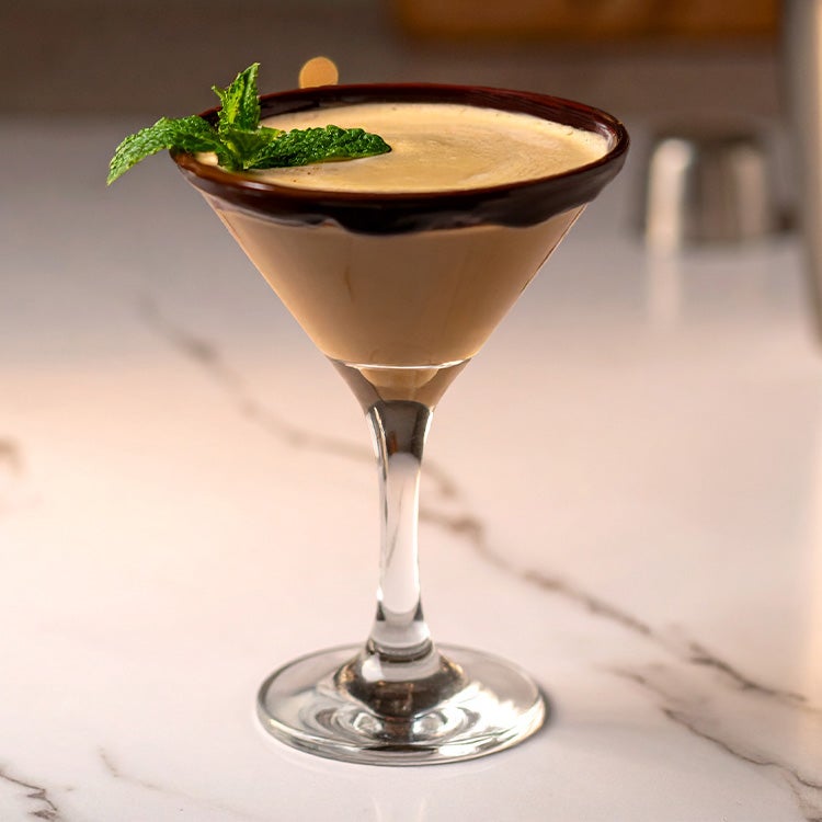 A creamy mint cocktail made with Irish Creme served in a Martini glass on a marble surface and garnished with a pinch of mint