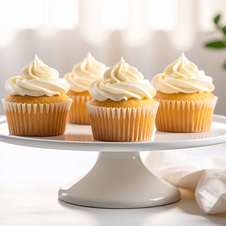 Four vanilla cupcakes on a cake tray topped with a swirl of Milkybar white chocolate buttercream, on a white surface
