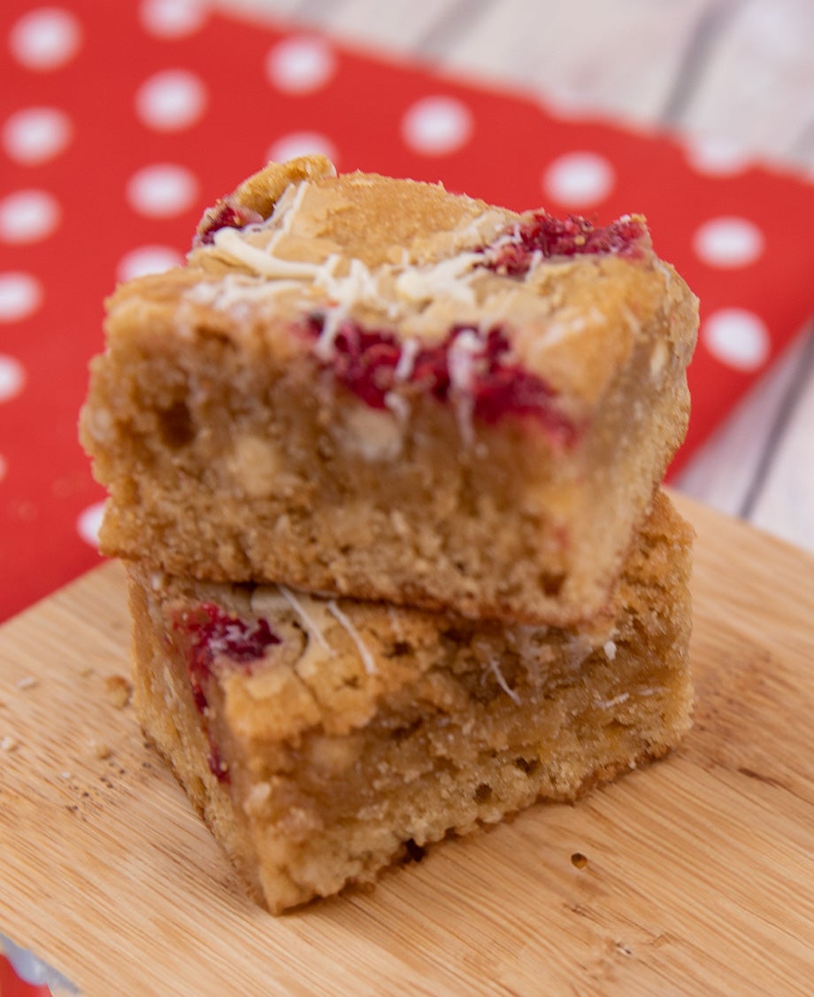 Close-up of White chocolate blondies studded with raspberry pieces pictured on a wooden board