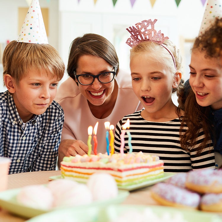 A group of children and a mum around a birthday cake about to blow out the candles
