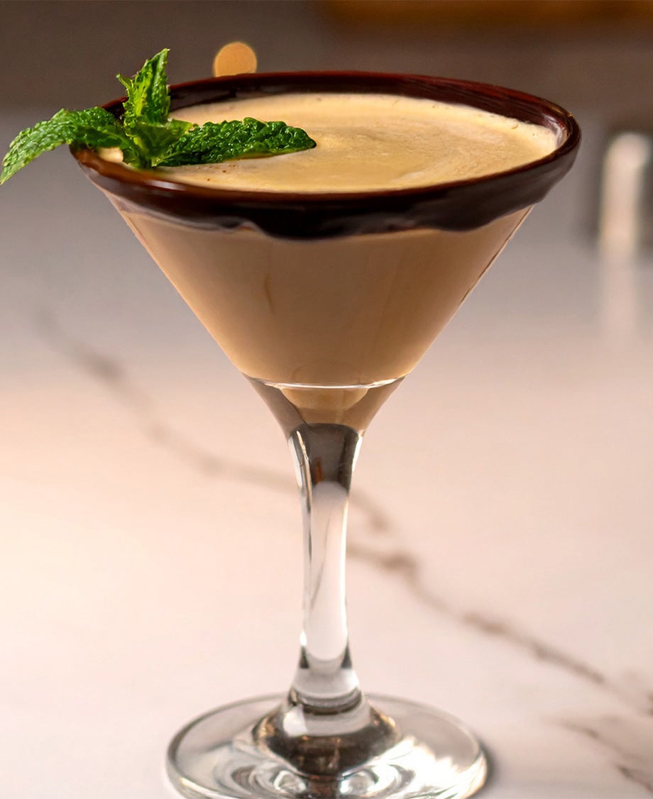 A creamy mint cocktail made with Irish Creme served in a Martini glass on a marble surface and garnished with a pinch of mint