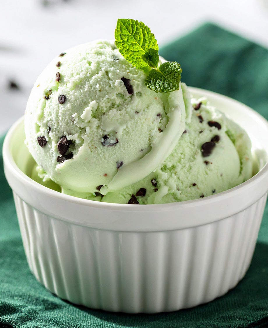 Two small scoops of chocolate and mint ice cream in a qhite ramekin, decorated with a sprig of mint