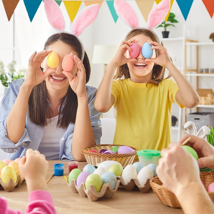 A family wearing bunny ears holds coloured eggs up to their faces