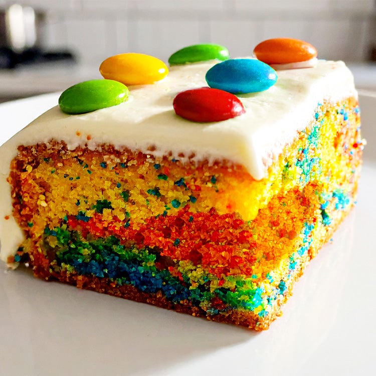 Square slice of a sponge cake with different coloured sections baked together with white buttercream icing