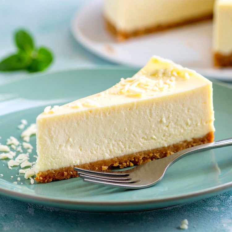 Slice of creamy Milkybar white chocolate cheesecake on a blue plate with a fork on it