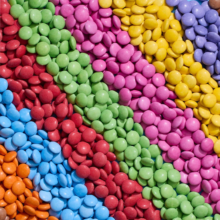 Rows of brown, orange, blue, red, green, pink, yellow and purple Smarties arranged by colour