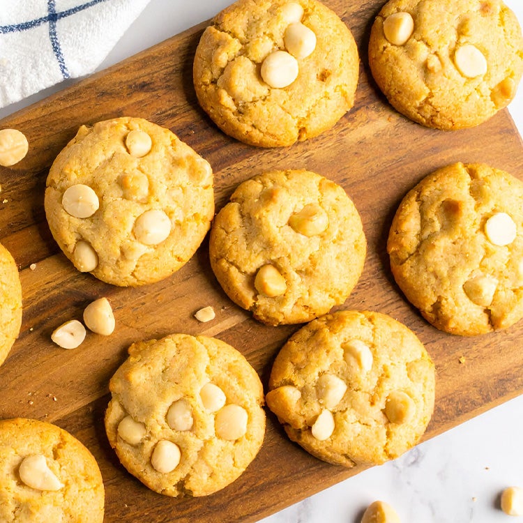 A wooden cutting board displaying a variety of freshly baked macadamia cookies arranged neatly.