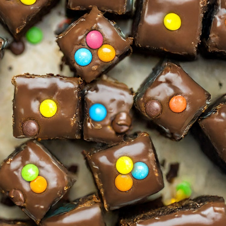 Small square chocolate brownie bakes topped with chocolate icing and colourful Smarties
