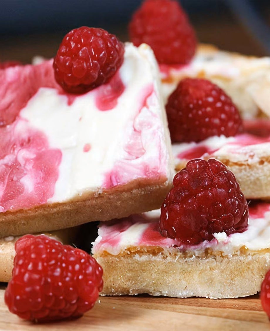 quares of pastry topped with Milkybar white chocolate and raspberry icing decorated with fresh raspberries, on a wooden board
