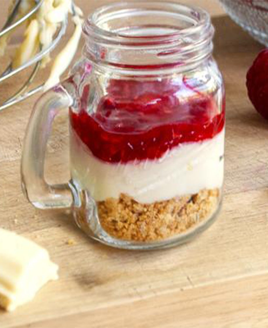 Glass jar of Milkybar white chocolate and raspberry cheesecakes on a wooden tabletop