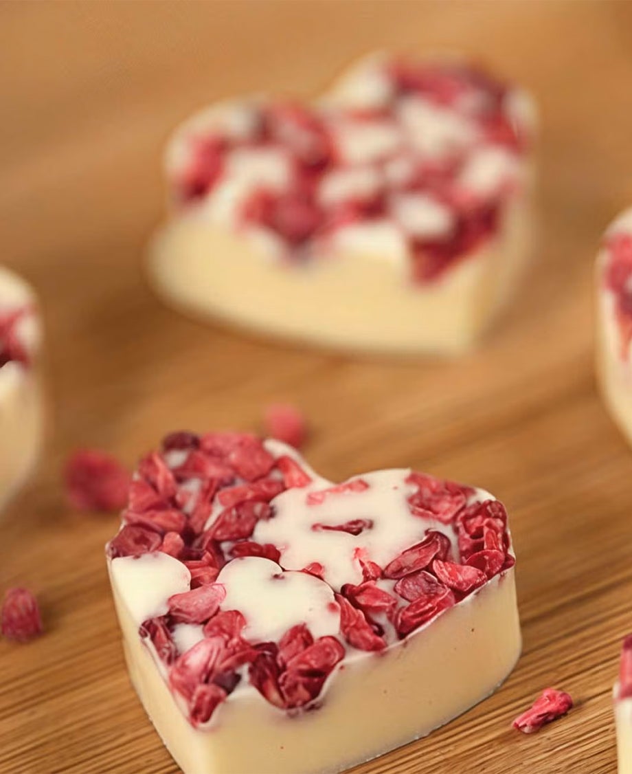 Milkybar white chocolate hearts decorated with freeze-dried raspberries on a wooden table top