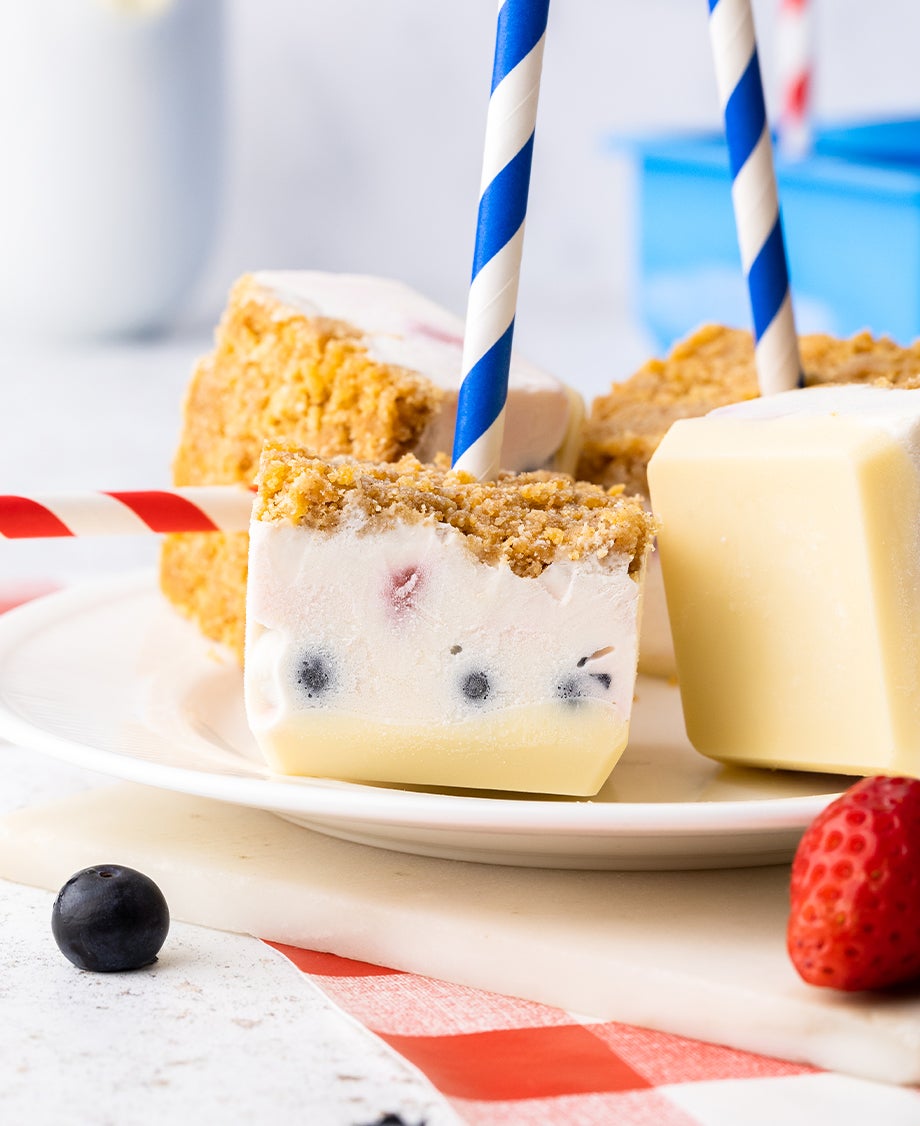 Square mini berry and white chocolate cheesecake pops on the end of paper straws arranged on a plate