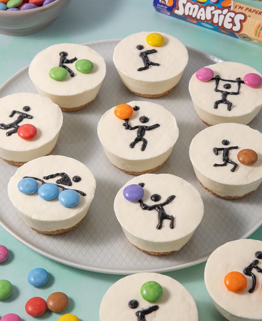 Round white mini cheesecakes with black line figures piped on and decorated with Smarties