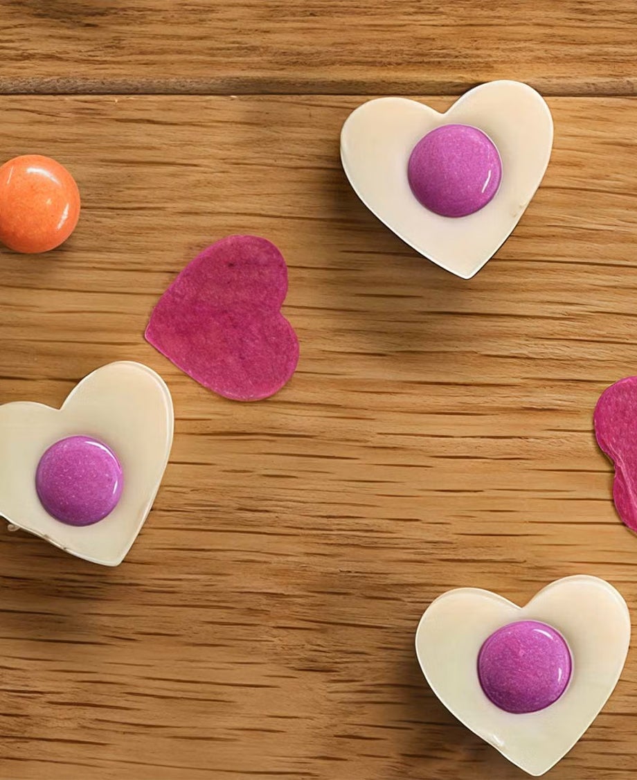 Milkybar white chocolate hearts decorated with one single Smartie at the centre on a wooden tabletop