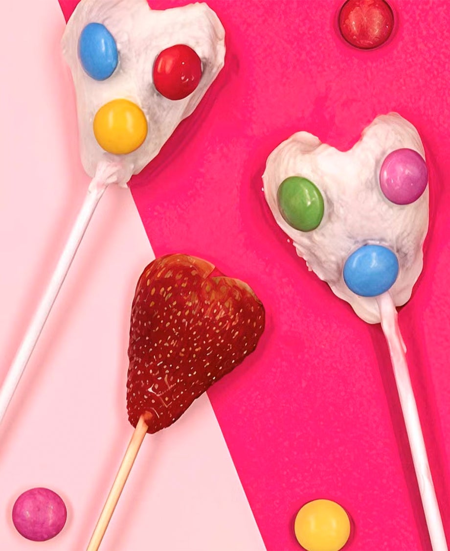 Strawberry lollipops made of fresh strawberry halves on sticks, coated with yoghurt and decorated with colourful Smarties