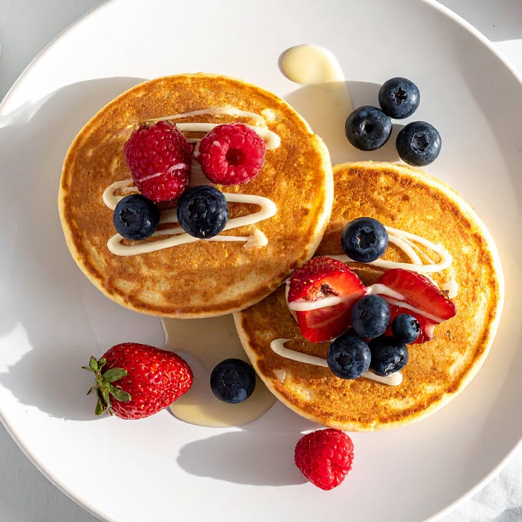 Plate of Scotch Pancakes on a marble worktop with fresh berries and drizzles of Milkybar white chocolate