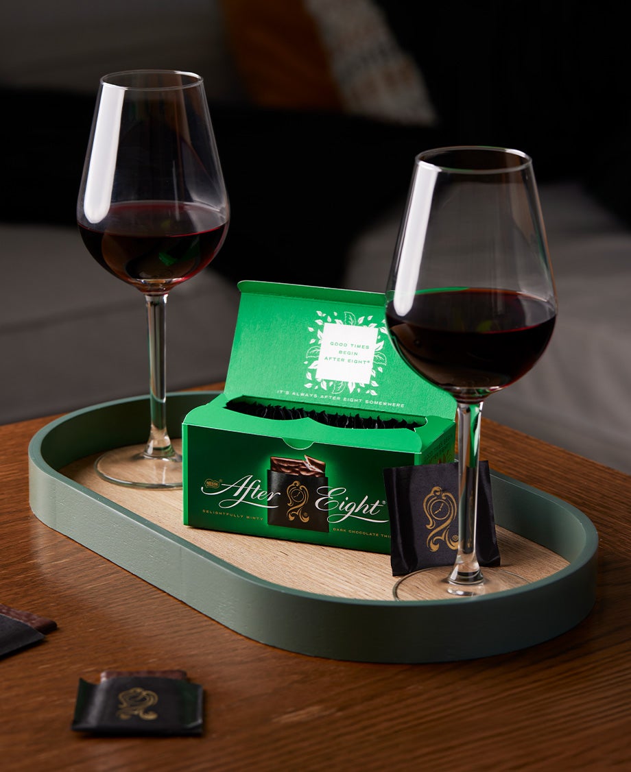 Box of After Eight mint chocolates on a stylish wooden tray with two glasses of red wine 