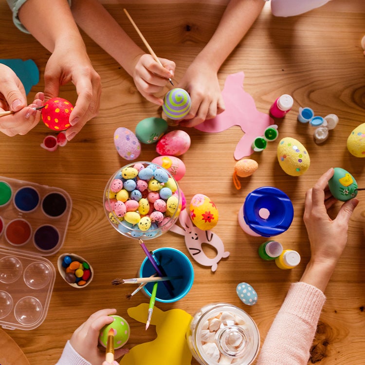 Overhead view of people painting and decorating colourful eggs around a wooden table