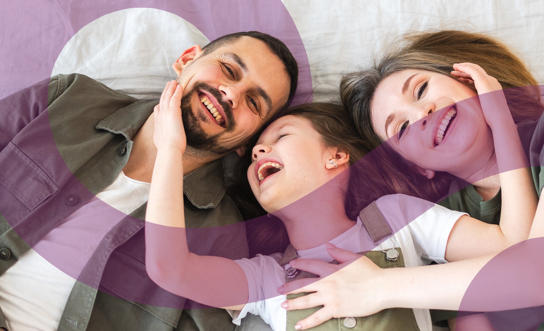 A girl lies between her mother and father sharing a joke together 